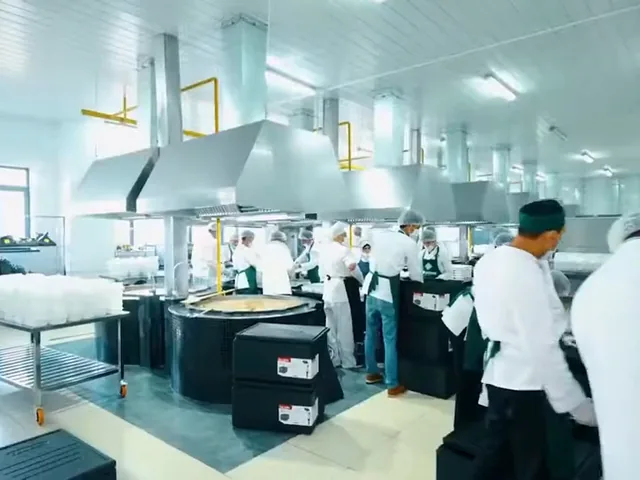 Commercial kitchen line where chefs prepare and plate food at cooking stations.