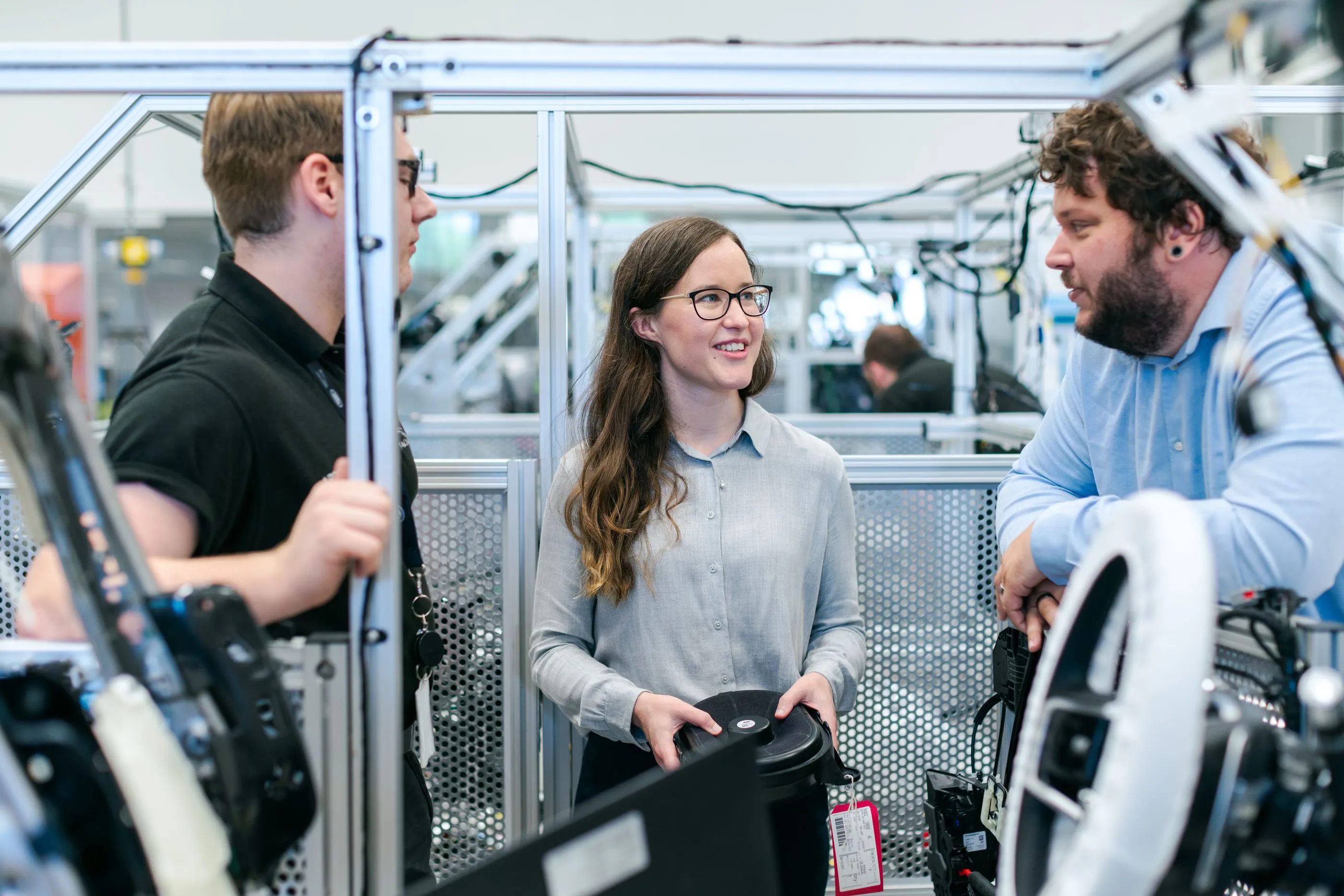 Three engineers talking between aluminium test rigs on a production floor