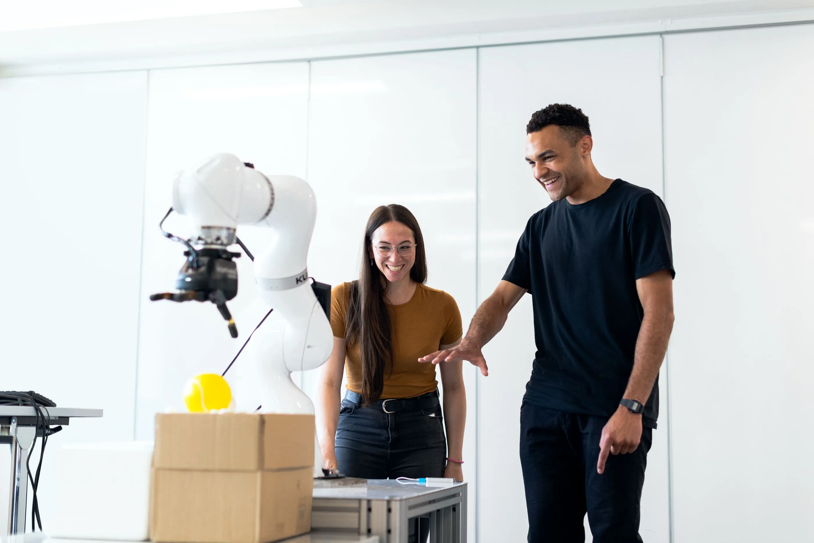 Two engineers testing a robot arm together in a bright lab